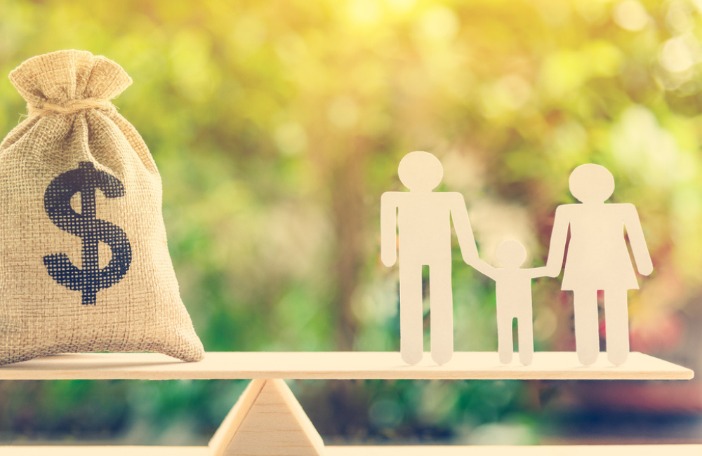 Money saving for kids, family financial wealth management concept : Dollar or cash in hemp bags or burlap sacks and a white paper cut (dad, mom and son) on wood balance scale. Green nature background.