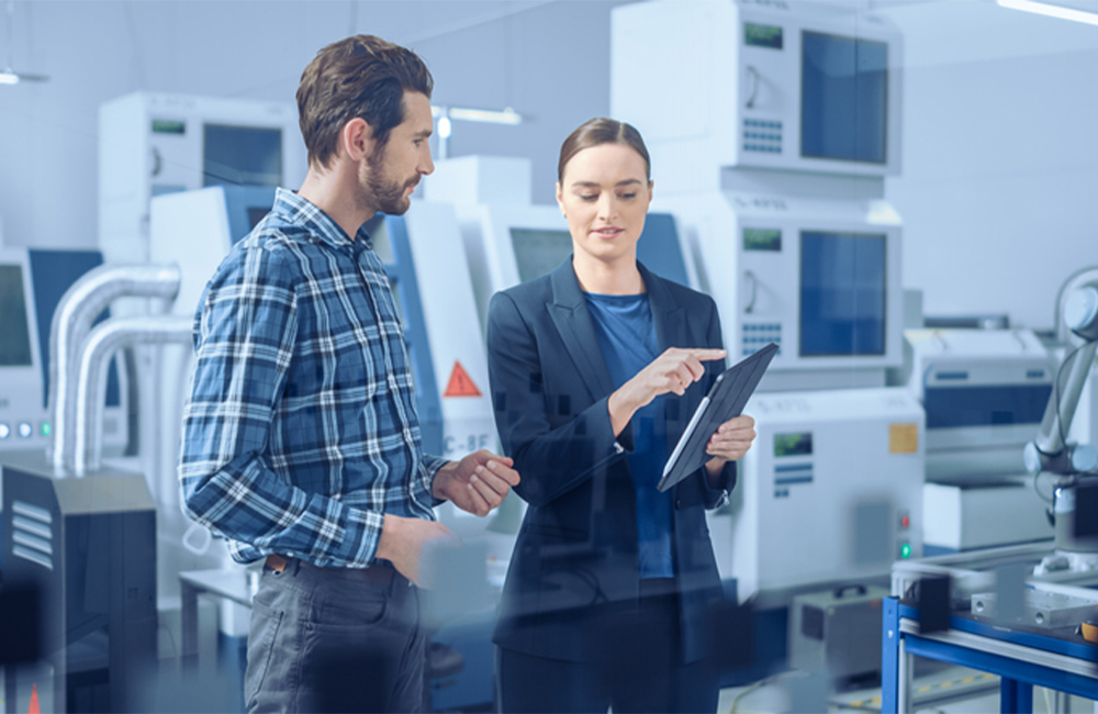 Modern Factory: Female Project Manager and Male Engineer Standing, Talking, Using Digital Tablet for Programming and Monitoring Assembly Line.