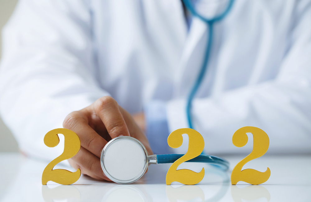 Doctor holding stethoscope near gold wooden number 2022 on desk. Idea for new trend in medicine treatment and diagnosis.