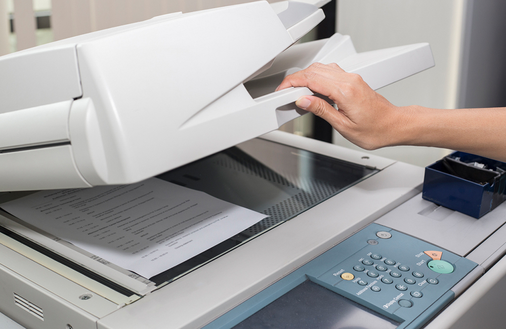 a woman's hand is closing a copier lid with a paper on the glass