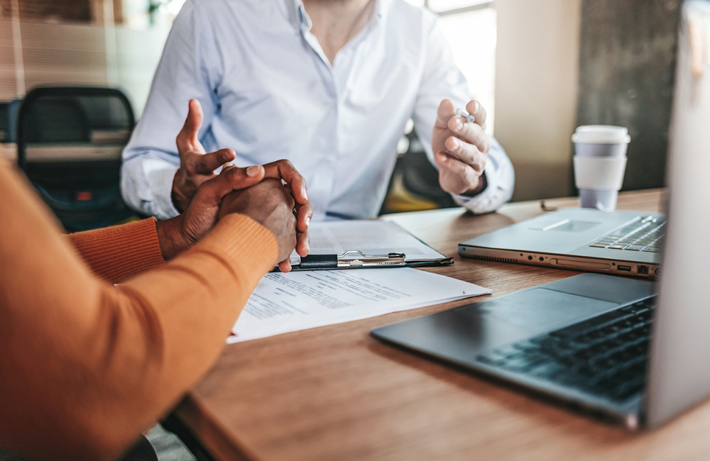 Couple reading legal documents at home with laptop, family considering mortgage loan or insurance, studying contract details, discussing terms and conditions, close up view of hands holding papers