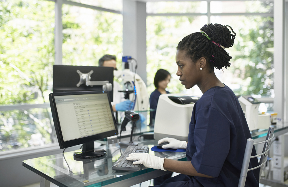 Close-up of African female pathology technician in late 20s examining data on desktop PC display in Buenos Aires clinical analysis laboratory.