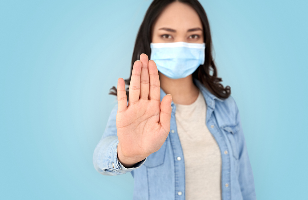 Concept of epidemic Chinese coronavirus. Confident young adult asian girl in safety face mask making stop sign, standing isolated on grey background with copy space
