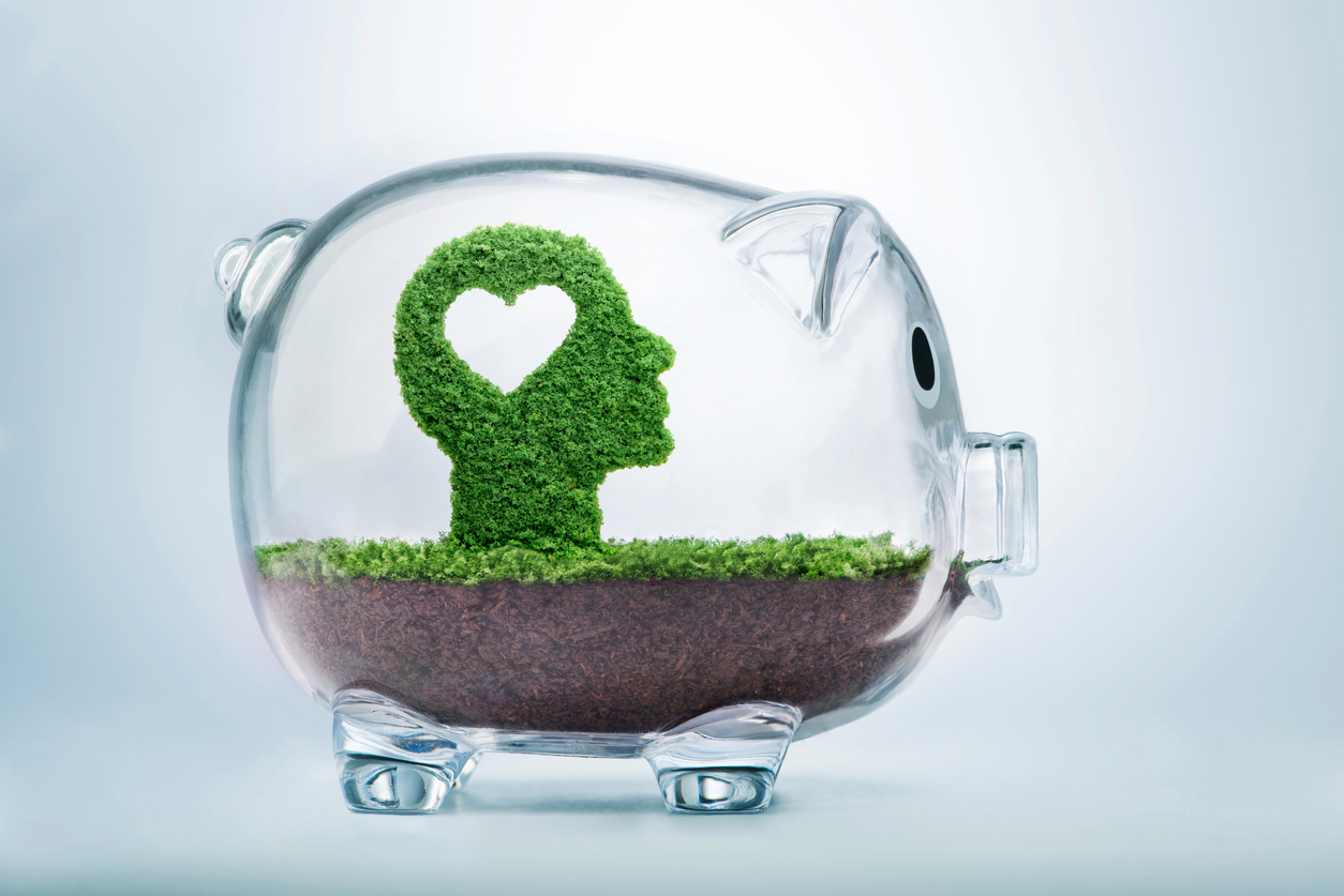 Love is the seed of our being. Grass growing in the shape of a cut out heart inside a human head, inside a transparent piggy bank, symbolising the care, dedication and investment needed for our love to grow.
