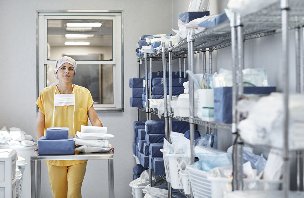 Confident surgeon with medical supplies on trolley. Female healthcare worker is in storage room. She is in hospital.