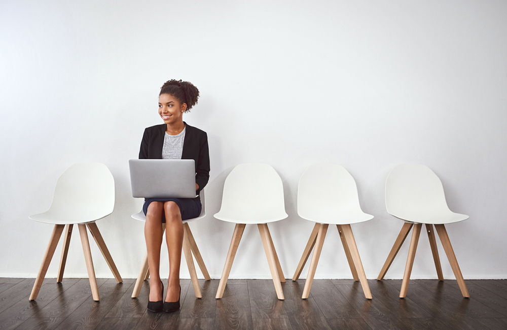 Studio shot of a young businesswoman using a laptop while waiting in line against a gray background