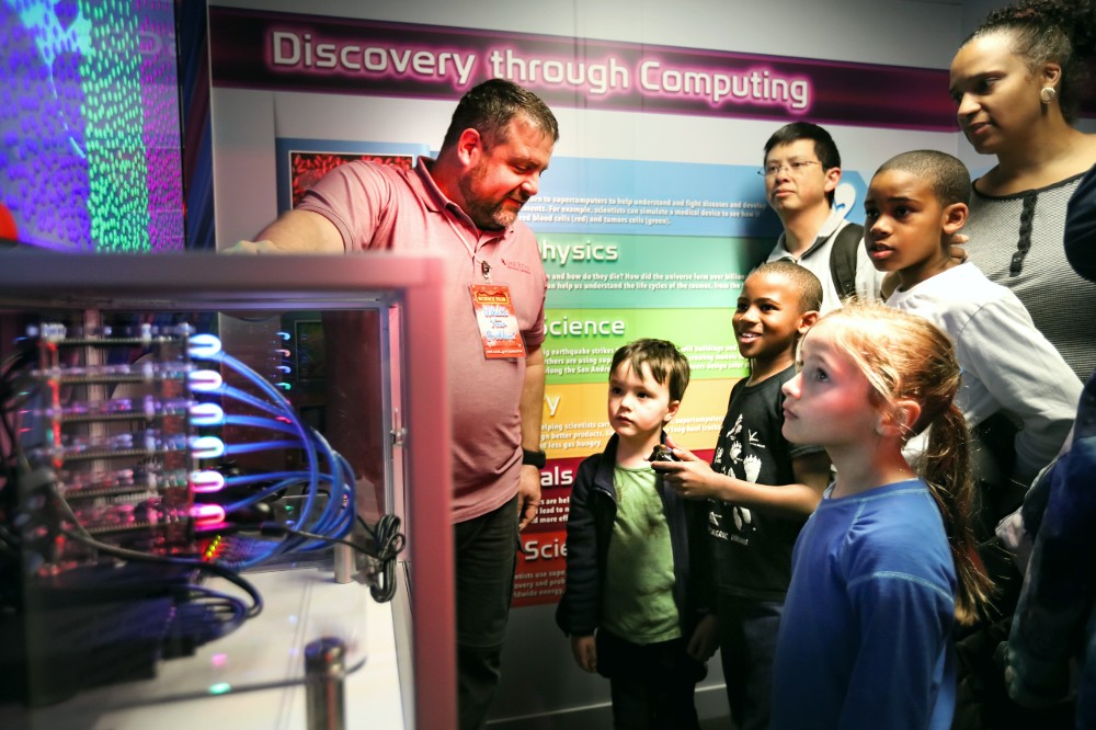 Researchers and kids look at a super computer